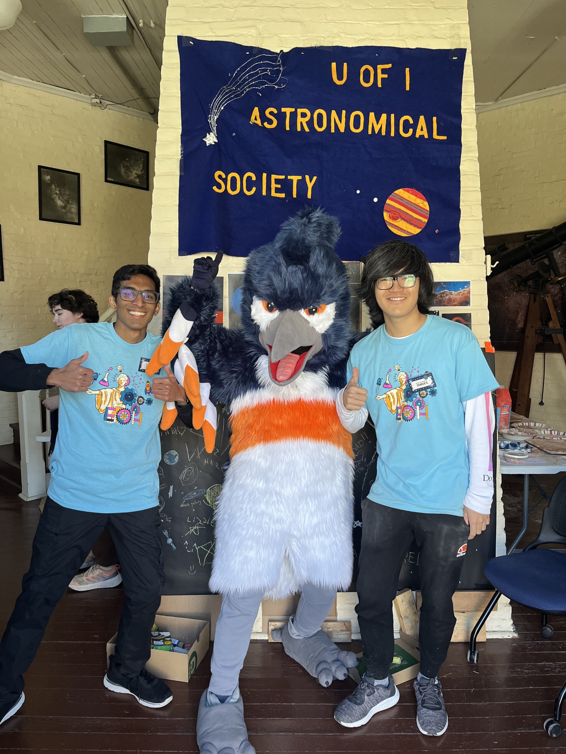 The Belted Kingfisher mascot posing next to students with a U of I Astronomical Society banner
