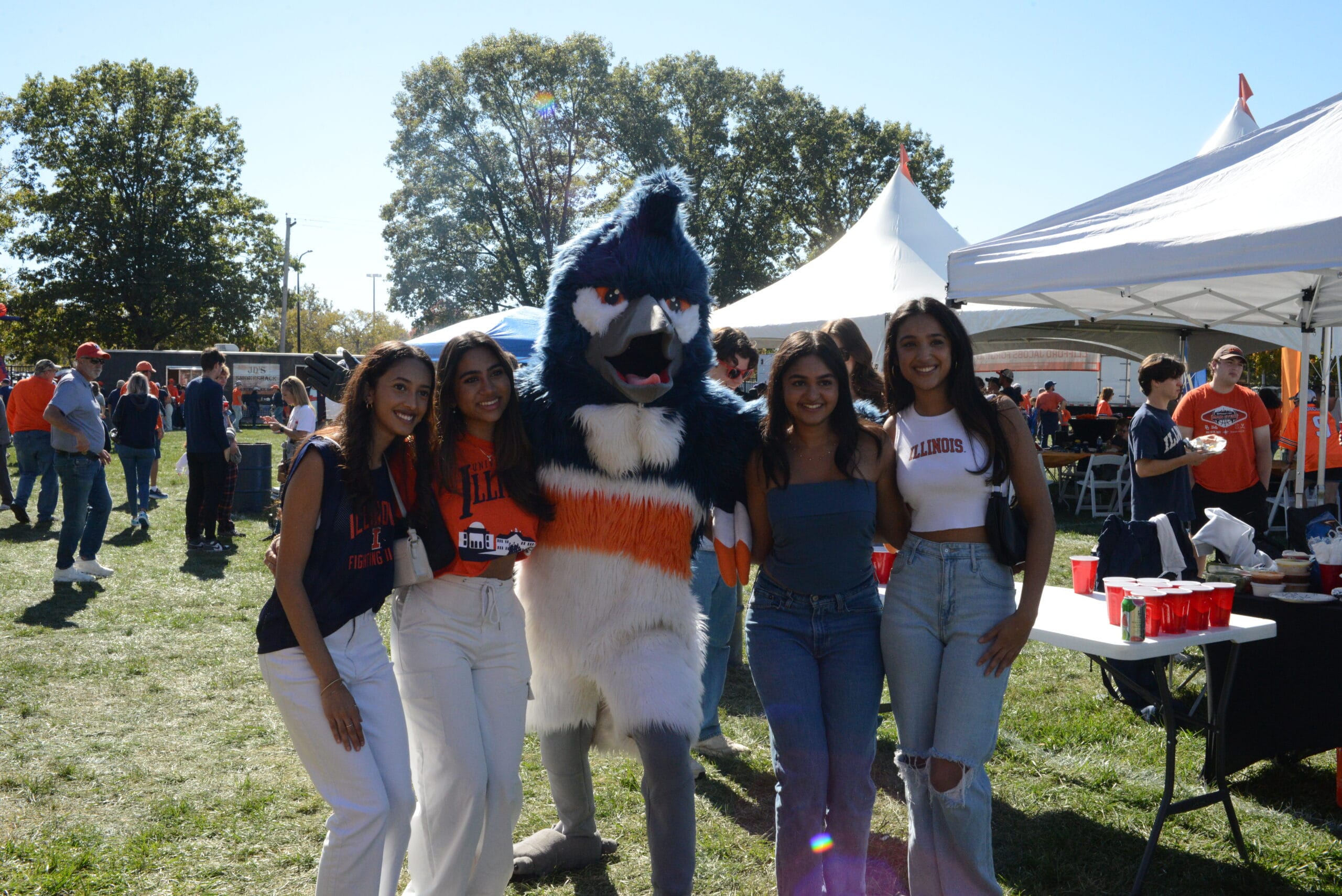 The Belted Kingfisher mascot posing with 4 students wearing orange and blue