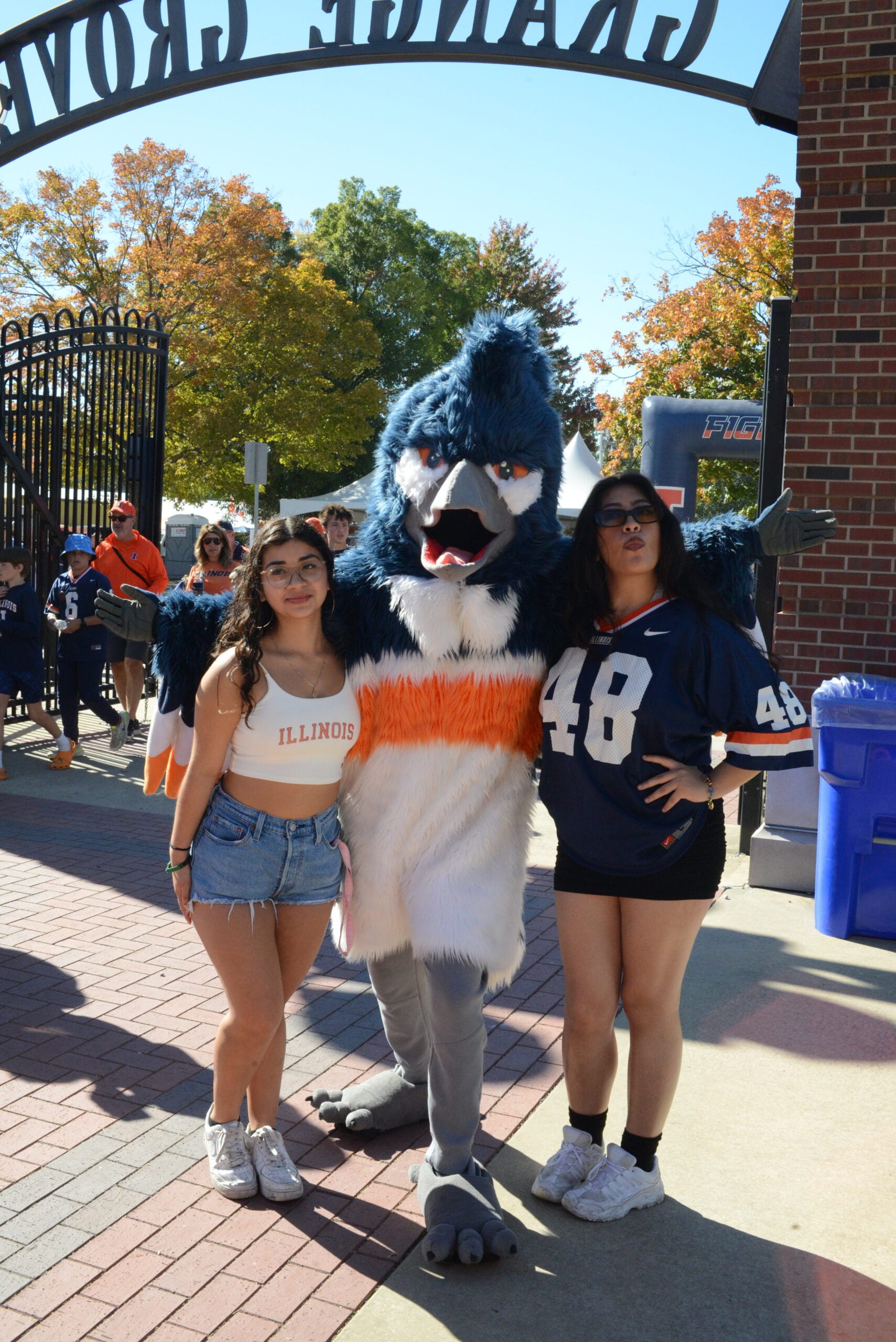 The Belted Kingfisher mascot posing together with two students wearing University of Illinois merchandise