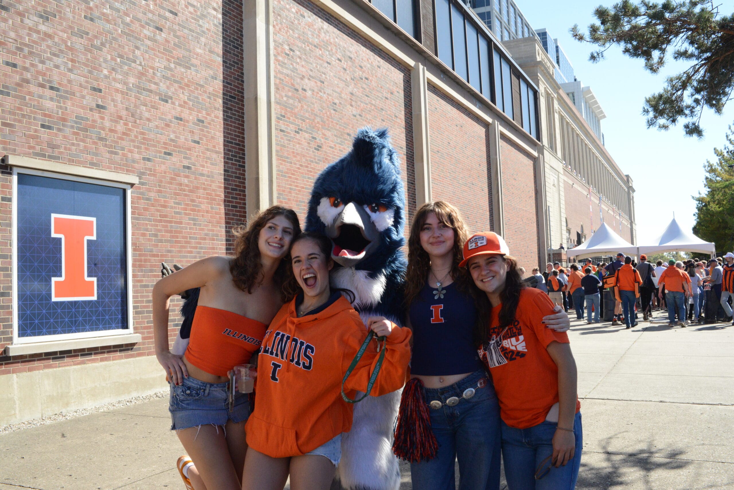 The Belted Kingfisher mascot posing together with four students wearing University of Illinois merchandise