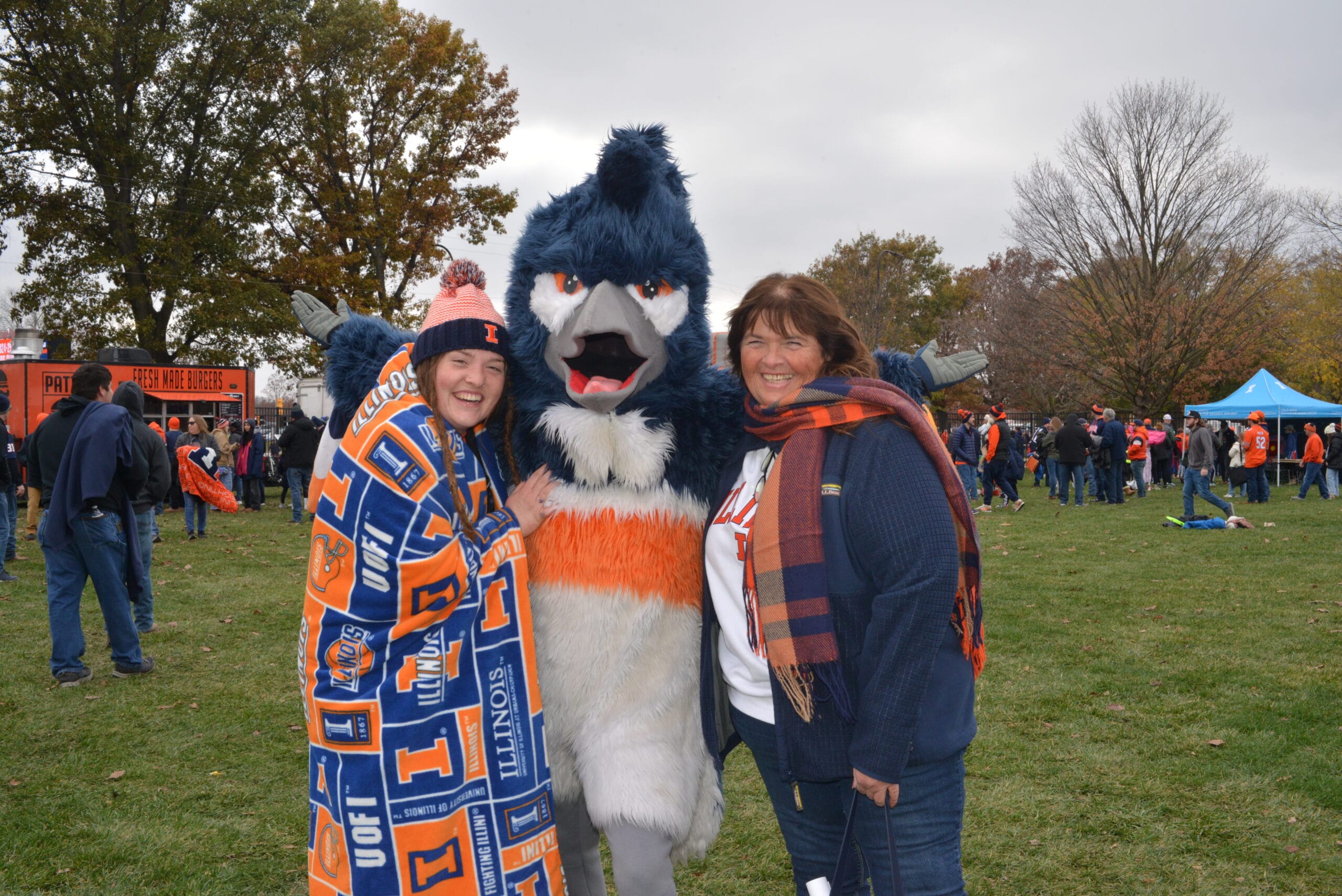 The Belted Kingfisher mascot posing together with two people wearing University of Illinois merchandise
