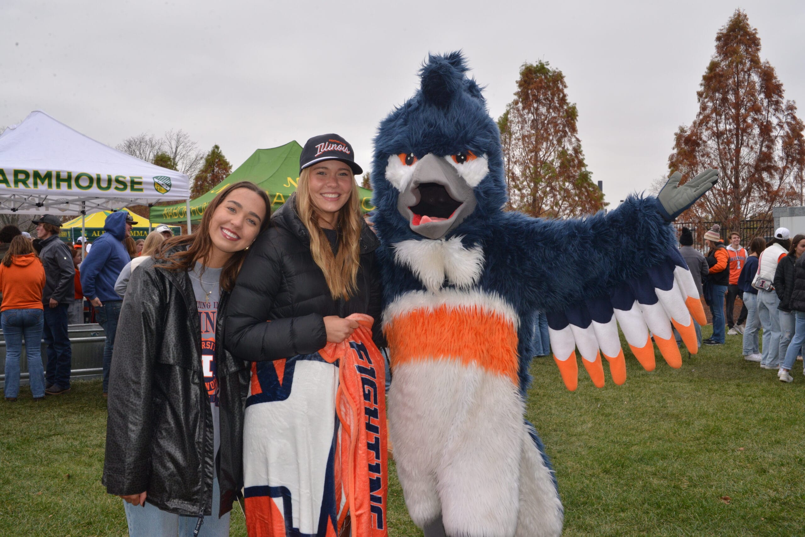 The Belted Kingfisher mascot posing together with two students wearing University of Illinois merchandise