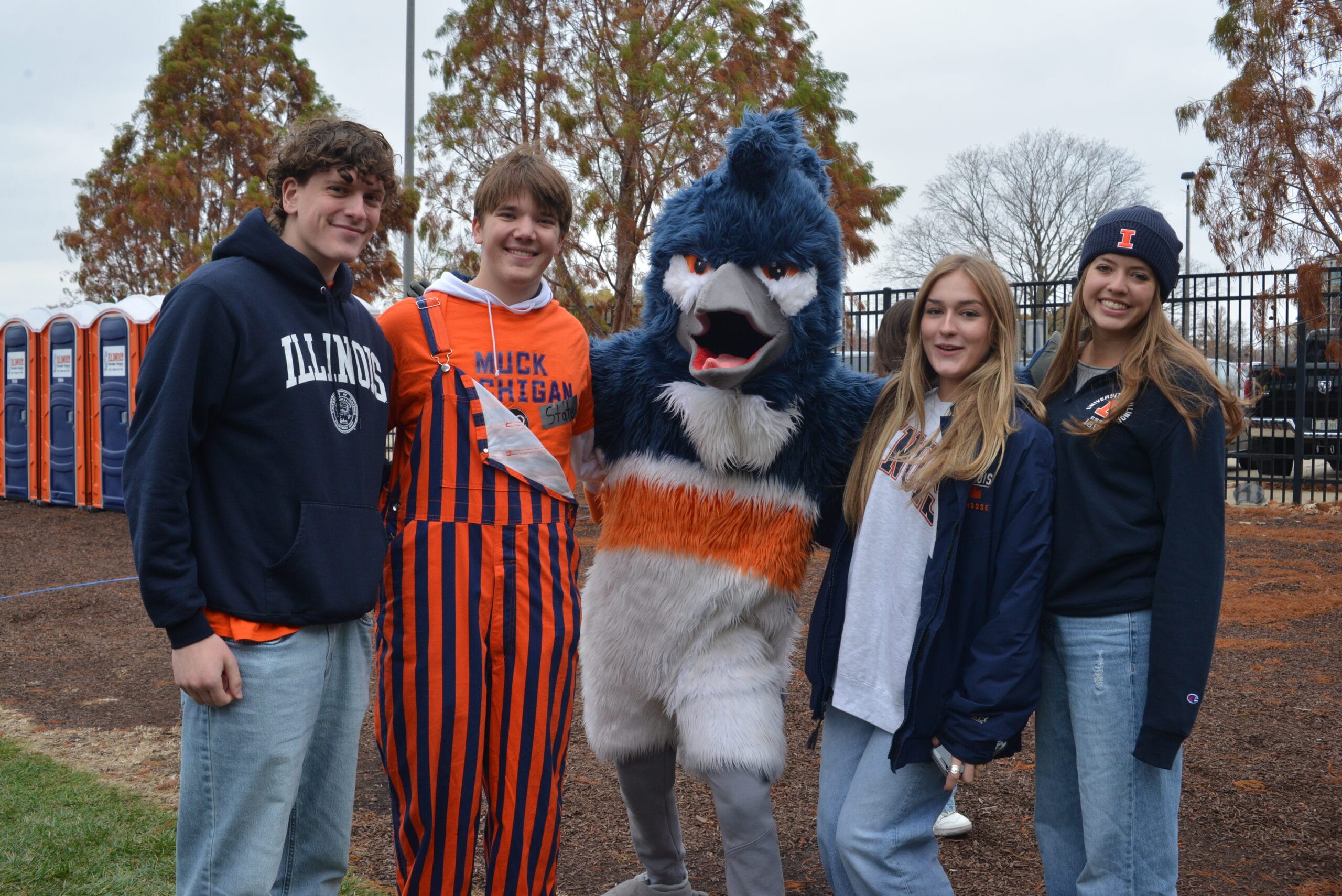 The Belted Kingfisher mascot posing together with four students wearing University of Illinois merchandise