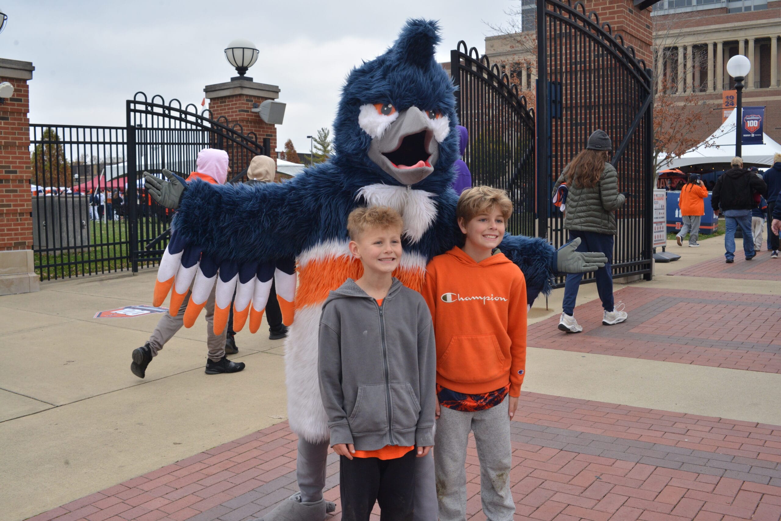 The Belted Kingfisher mascot posing together with two children wearing University of Illinois merchandise