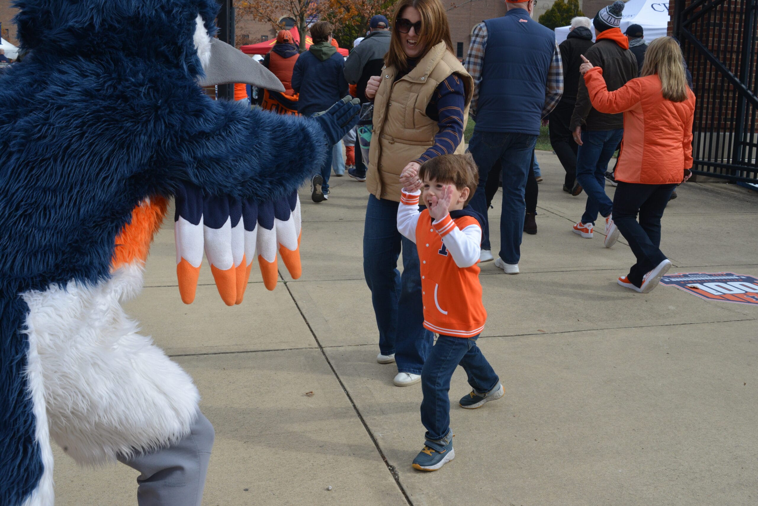 The Belted Kingfisher mascot about to high five a boy wearing a University of Illinois jacket