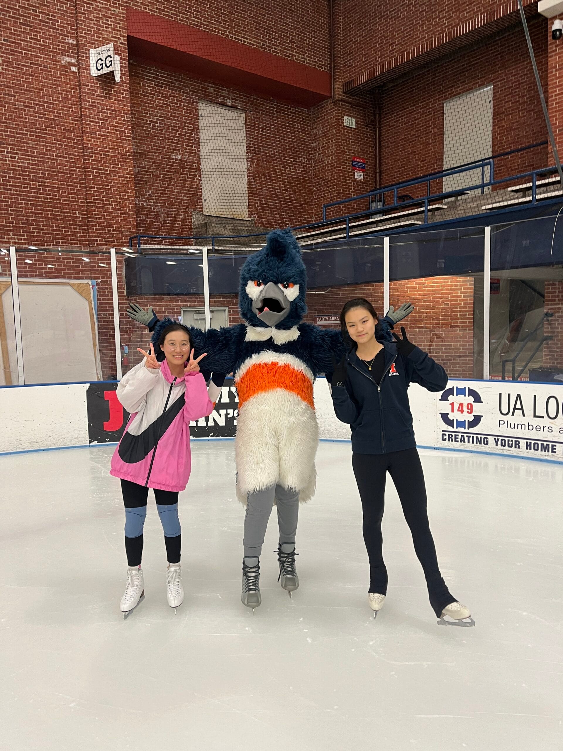 The Belted Kingfisher mascot posing with two students in the ice rink