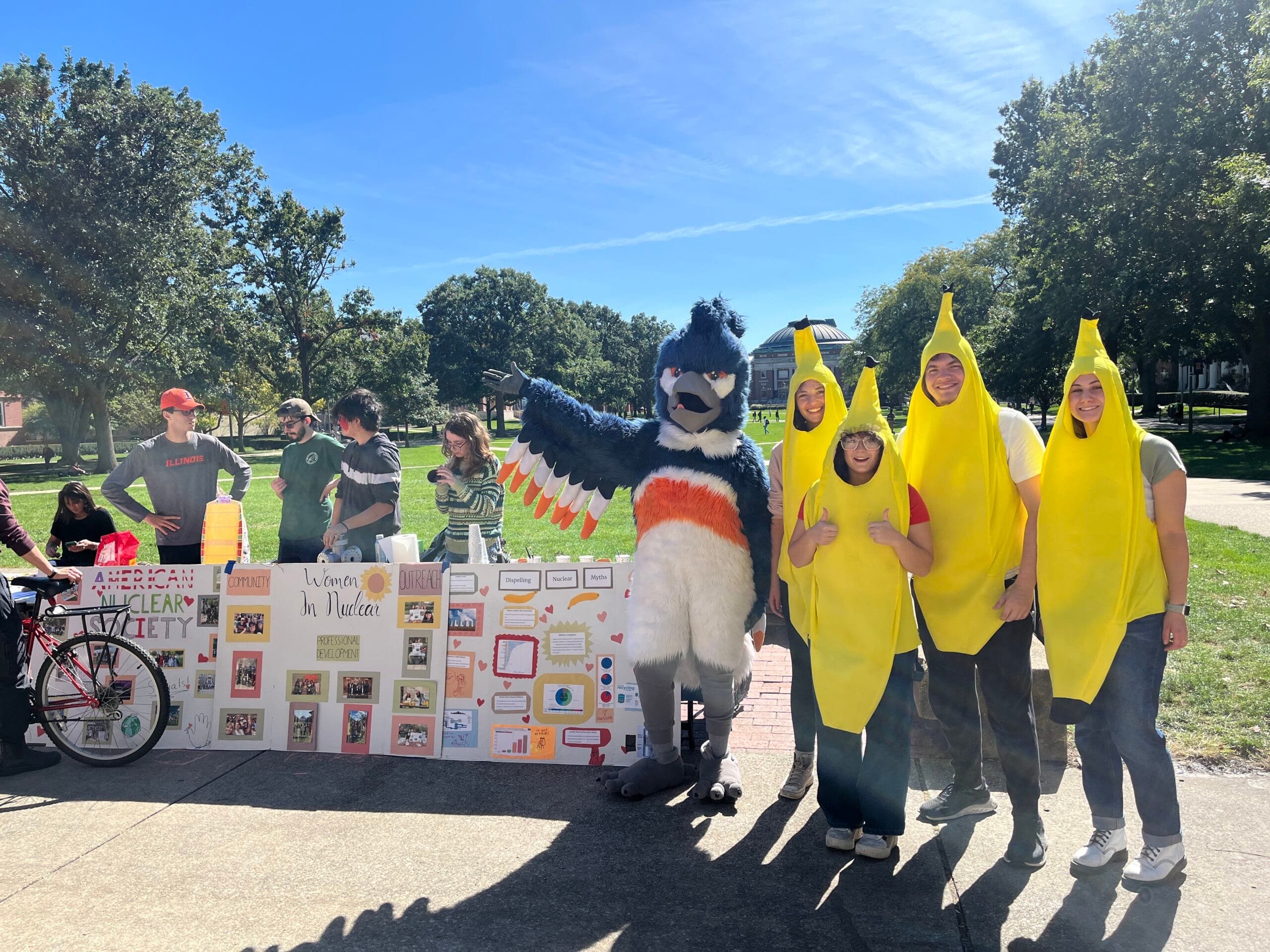 The Belted Kingfisher posing together with 4 students in banana suits next to the American Nuclear Society booth