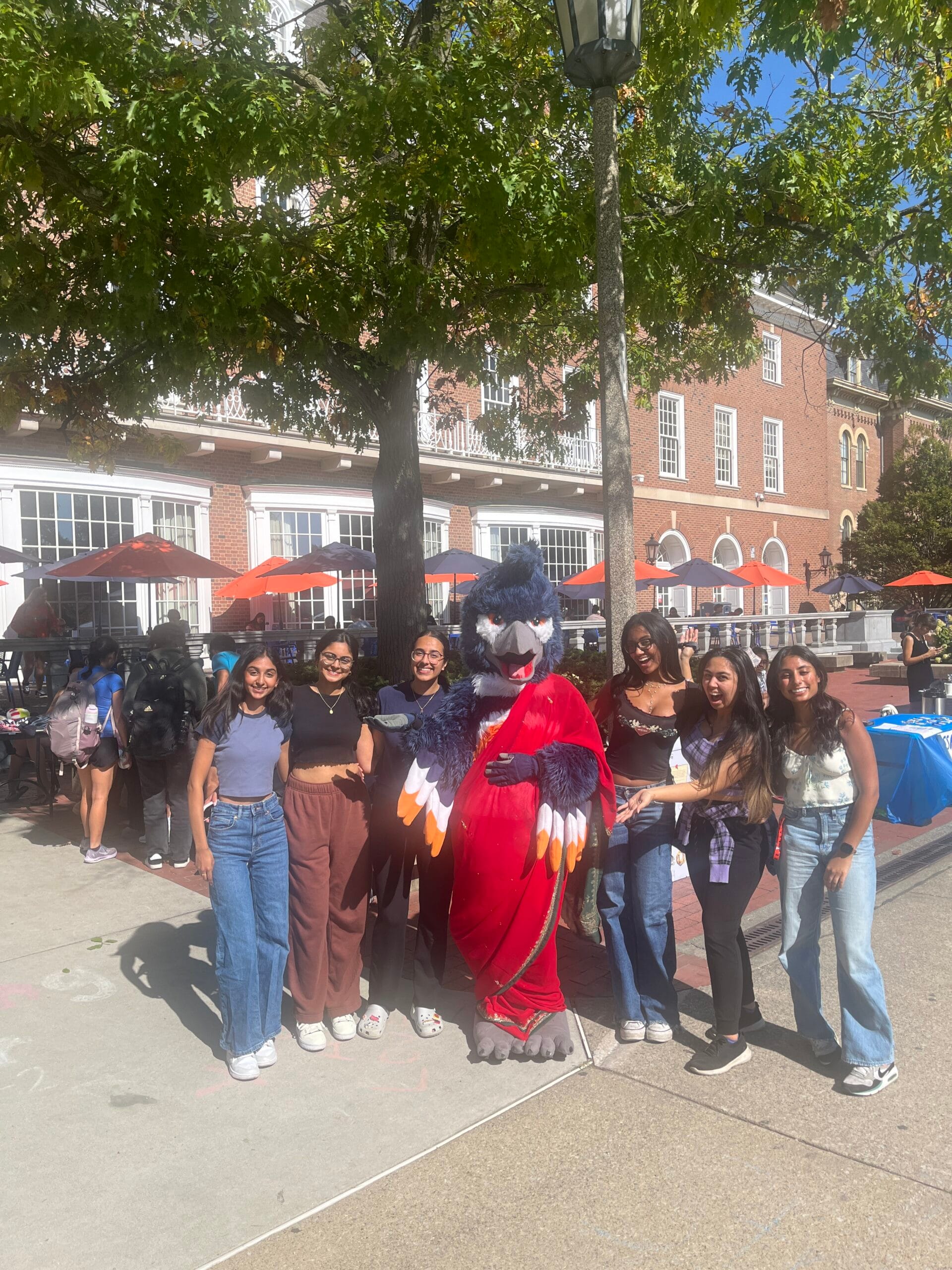 The Belted Kingfisher mascot posing in a red sari with 6 students