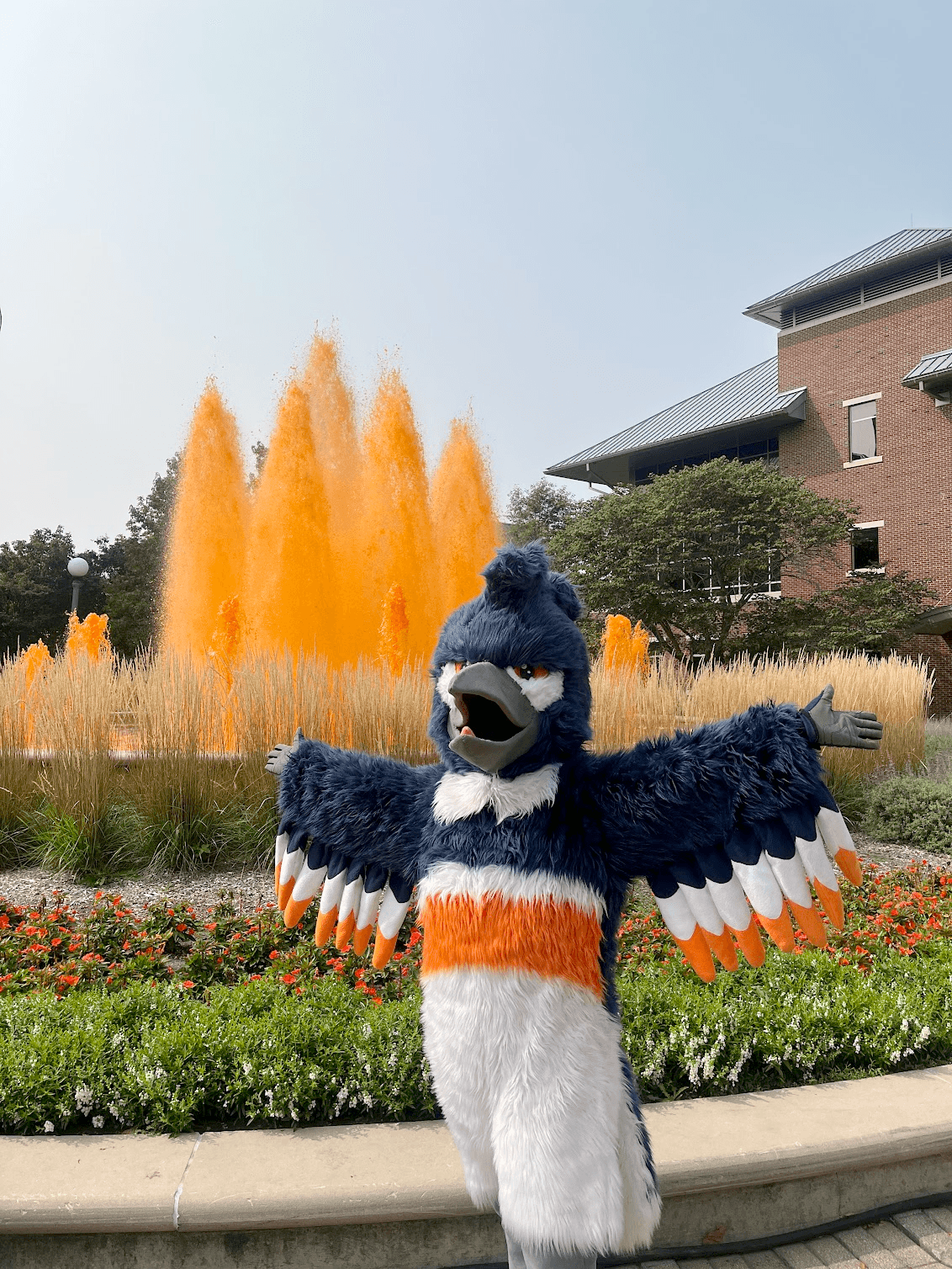 The Belted Kingfisher mascot posing in front of an orange fountain