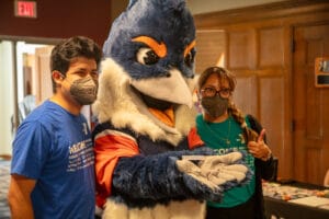Belted Kingfisher holding up a tag that reads "New American Welcome Center" between two people