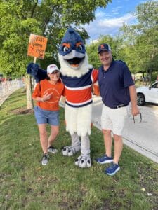 Belted Kingfisher posing between two adults. One of them is holding up a sign that reads "Run Maeve Run".