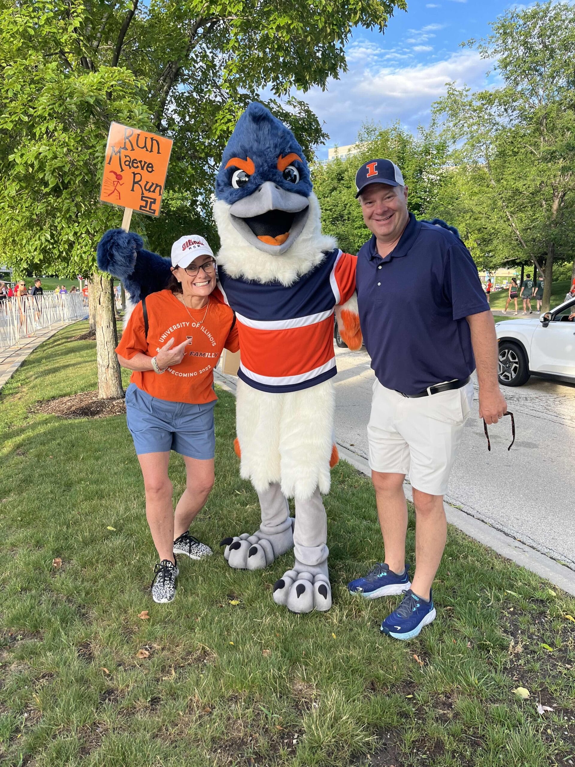 Belted Kingfisher posing between two adults. One of them is holding up a sign that reads "Run Maeve Run".