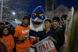 The Belted Kingfisher mascot posing with several University of Illinois students on Green Street. One of the students holding up a Daily Illini Newspaper that reads "Final Four"